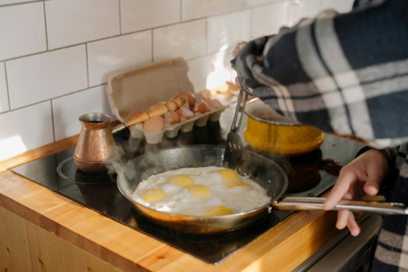 Person cooking sunny-side-up eggs on a stovetop with steam rising