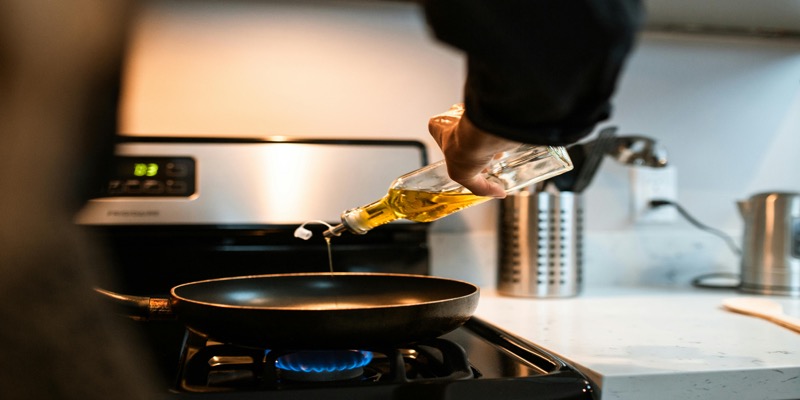 Hand pouring golden olive oil from bottle into cooking pan on stovetop