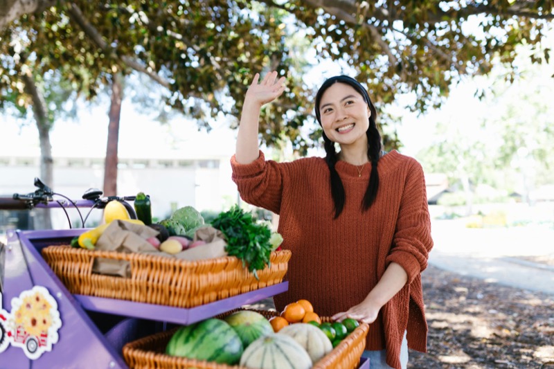 Smiling woman with fresh produce on purple cargo bike representing healthy lifestyle and wellness